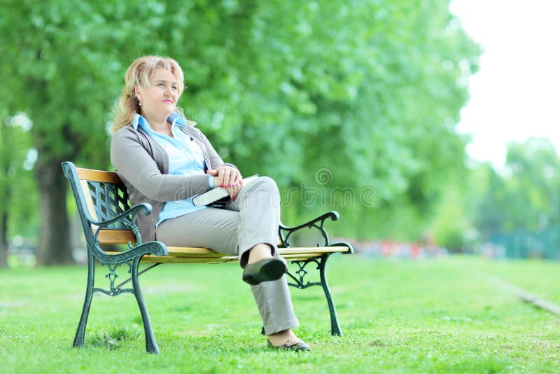 Senhora madura que relaxa em um parque assentado em um banco fotografia de stock royalty free Senhora madura que relaxa em um parque assentado em um banco fotografia de stock royalty free