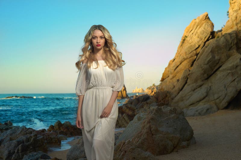 Beautiful lady in white dress on rocky shore. Beautiful lady in white dress on rocky shore