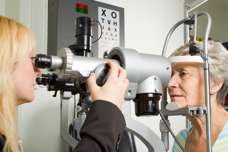 An older lady taking an eyesight test examination at an optician clinic. An older lady taking an eyesight test examination at an optician clinic