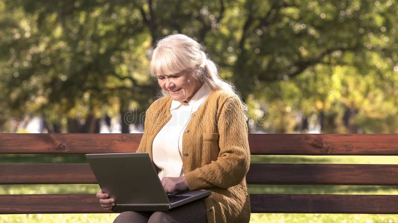 Senhora superior que trabalha no laptop fora no parque, tecnologia da informação foto de stock royalty free Senhora superior que trabalha no laptop fora no parque, tecnologia da informação foto de stock royalty free