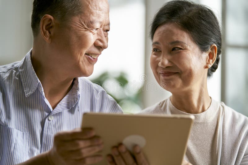 Happy senior asian couple sitting on couch at home using digital tablet together. Joyful loving elderly couple stock images, royalty-free photos and pictures