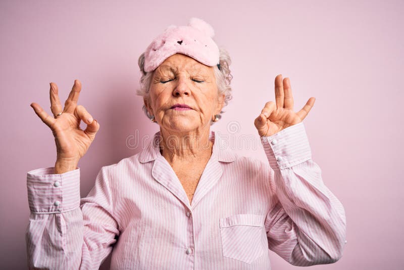 Senior beautiful woman wearing sleep mask and pajama over isolated pink background relax and smiling with eyes closed doing