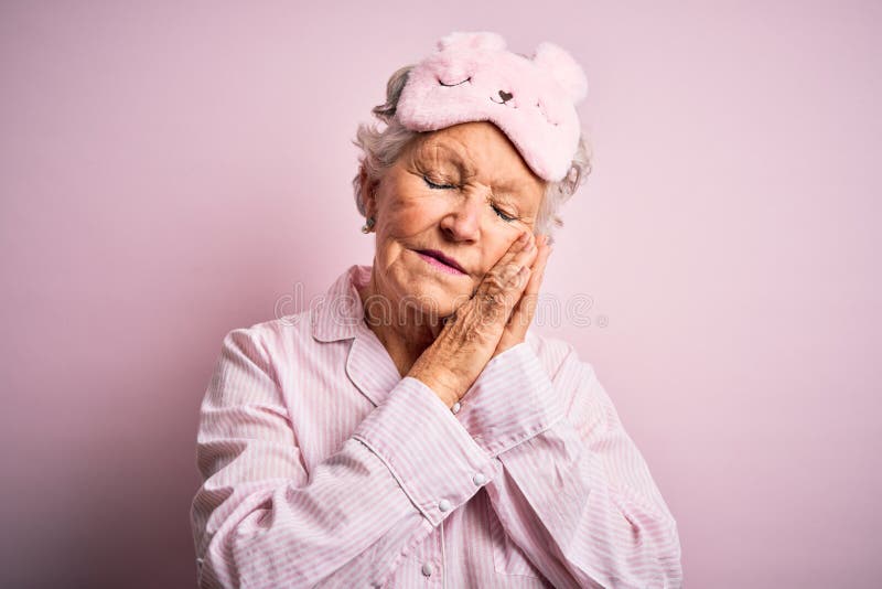 Senior beautiful woman wearing sleep mask and pajama over isolated pink background sleeping tired dreaming and posing with hands