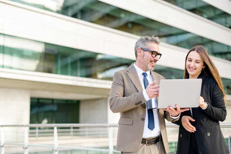 A senior businessman and a younger female colleague engage with content on a laptop together stock photography