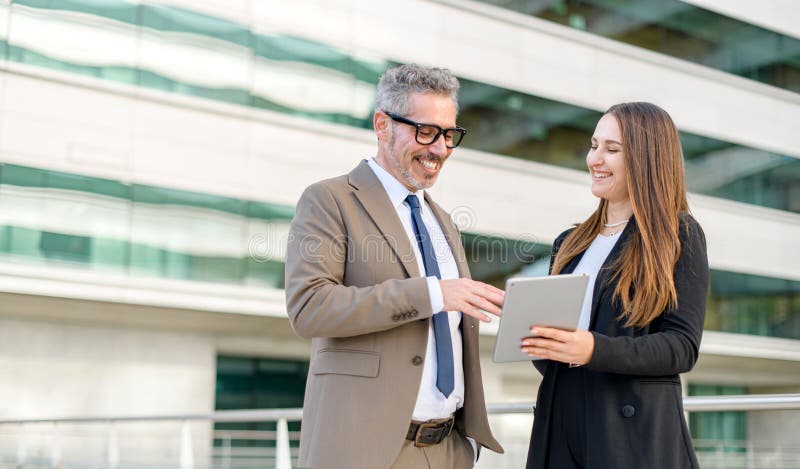 A senior businessman and a younger female colleague engage with content on a tablet together stock photos