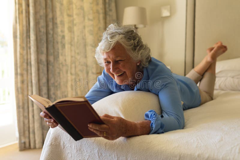 Senior caucasian woman lying in bed and reading book in bedroom