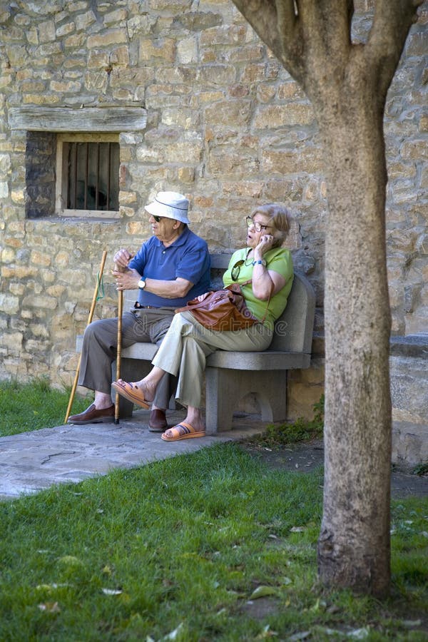 Senior citizens resting and making cell phone call on Plaza Mayor, in Ainsa, Huesca, Spain in Pyrenees Mountains, an old walled to