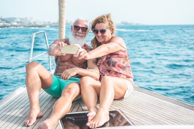 Senior couple doing selfie on sailboat during luxury ocean trip vacation - Old trendy people having fun on exclusive holiday -