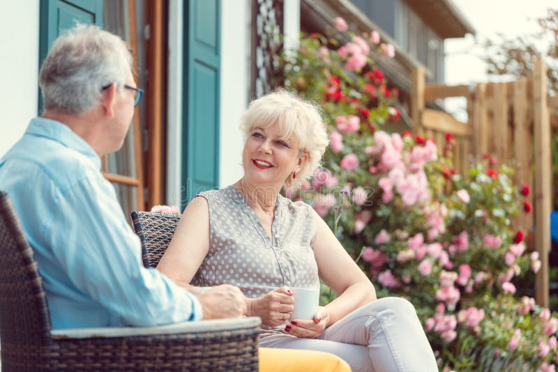 Senior couple enjoying their coffee sitting on porch in front of their house