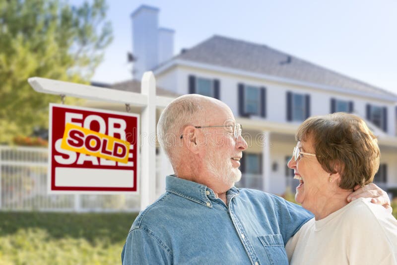 Happy Affectionate Senior Couple Hugging in Front of Sold Real Estate Sign and House. Happy Affectionate Senior Couple Hugging in Front of Sold Real Estate Sign and House.