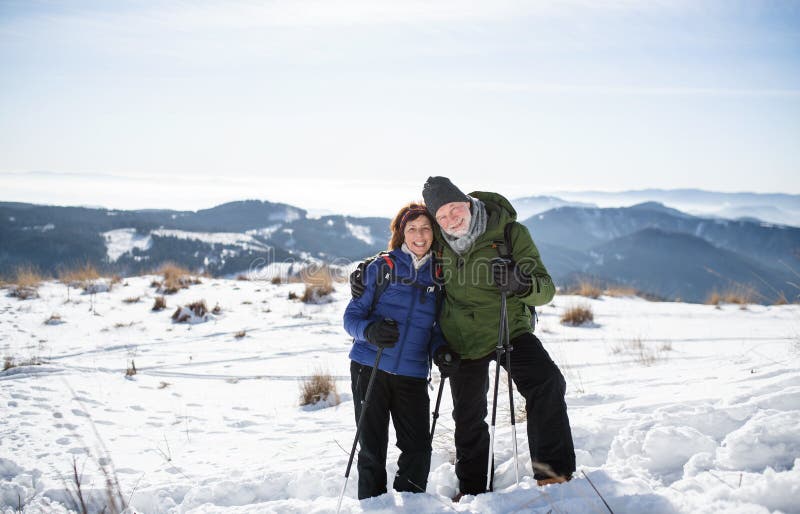 Senior couple hikers with nordic walking poles in snow-covered winter nature.