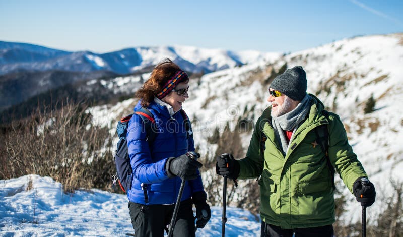 Senior couple hikers with nordic walking poles in snow-covered winter nature.