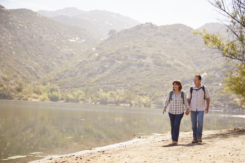 Senior couple hold hands hiking by mountain lake, front view royalty free stock images