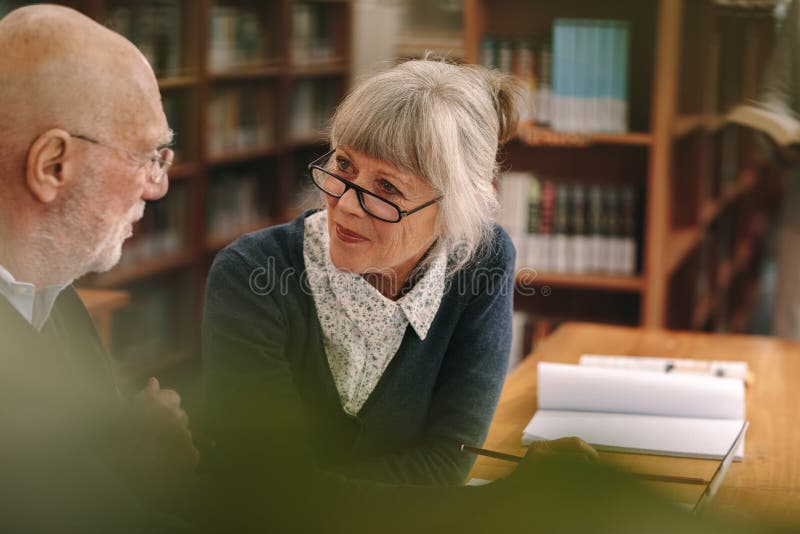 Senior couple interacting with each other sitting in a library royalty free stock photo Senior couple interacting with each other sitting in a library royalty free stock photo