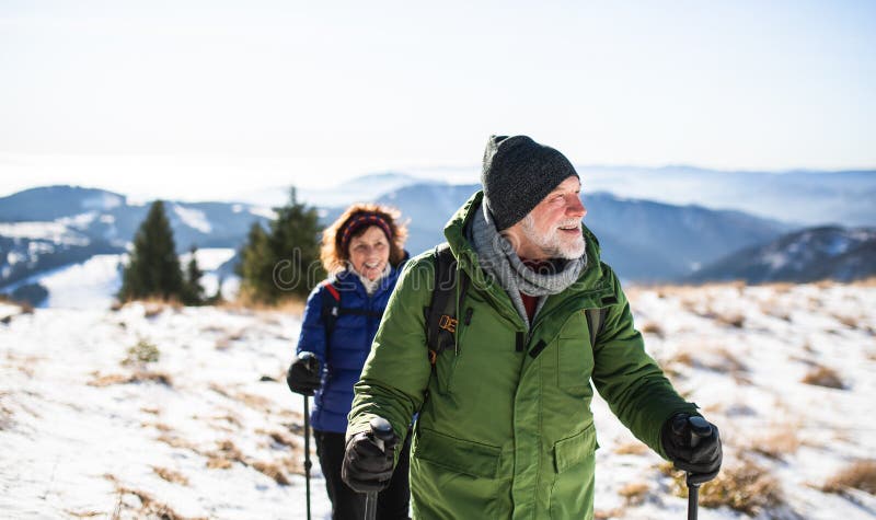 Senior couple with nordic walking poles hiking in snow-covered winter nature.