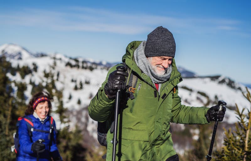 Starší pár s holemi pro nordic walking turistika v zasněžené zimní přírodě.