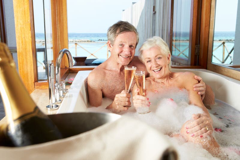 Mature couple kissing while drinking champagne inside their bathroom stock photo