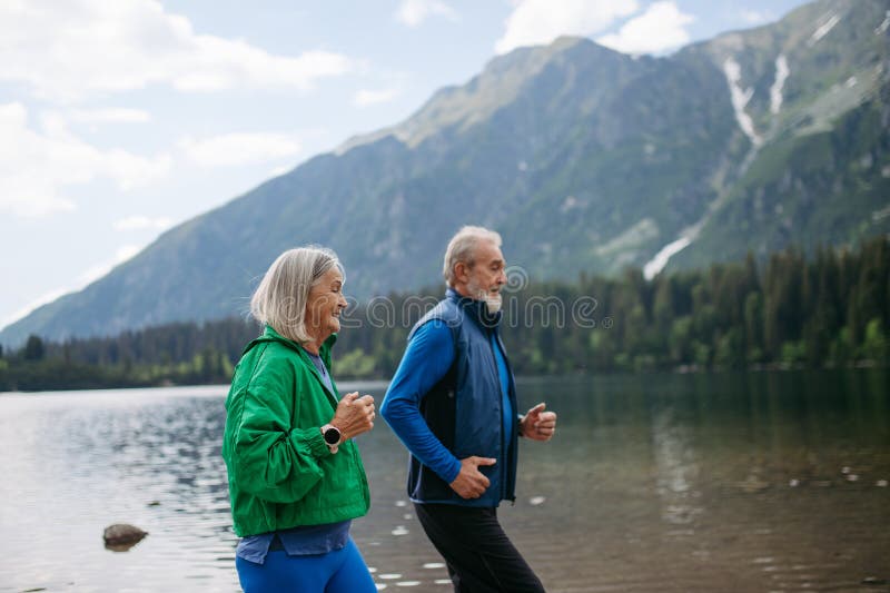 Senior couple running by the lake in the mountains.