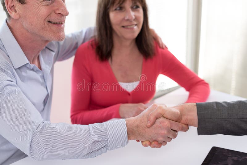 Female realtor handshaking happy mature couple