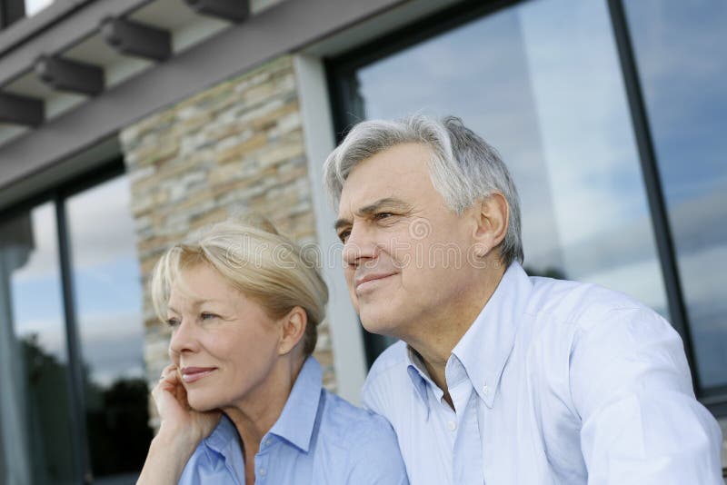 Senior couple sitting in front of house and looking away. Senior couple sitting in front of house and looking away