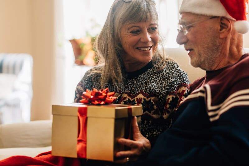 Senior couple sitting at home celebrating christmas holding a gi stock photos Senior couple sitting at home celebrating christmas holding a gi stock photos
