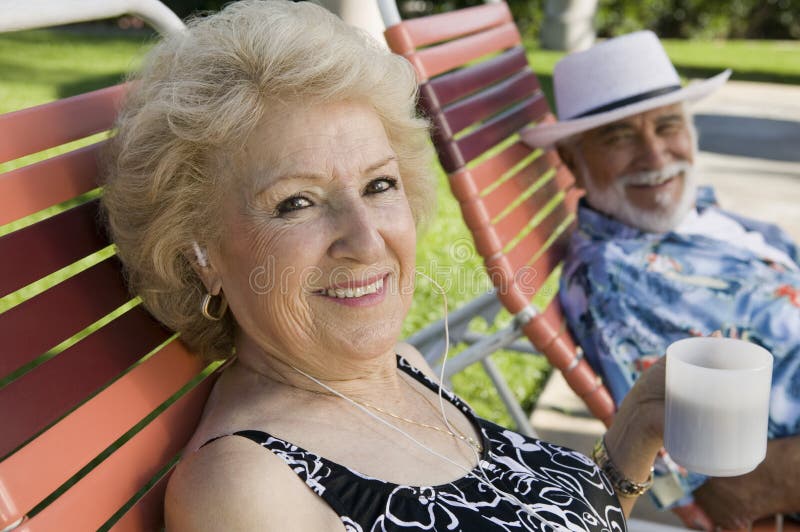 Senior Couple sitting on lawn chairs woman listening to earphones and holding cup portrait.