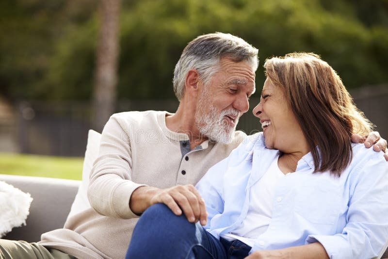 Senior Couple Sitting on a Seat in the Garden, Heads Turned Smiling To ...