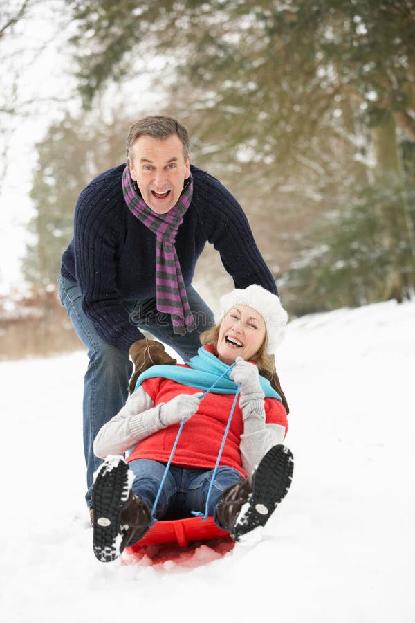 Senior Couple Sledging Through Snowy Woodland