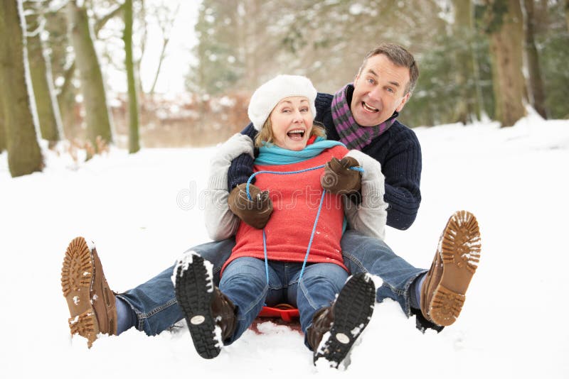 Senior Couple Sledging Through Snowy Woodland