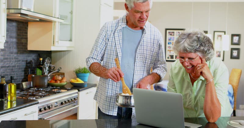 Senior couple using laptop while cooking in kitchen 4k