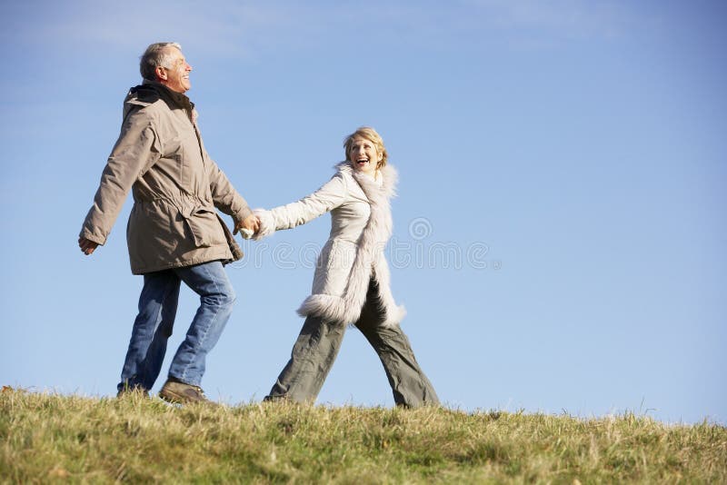 Senior Couple Walking In Park Wearing Winter Coats