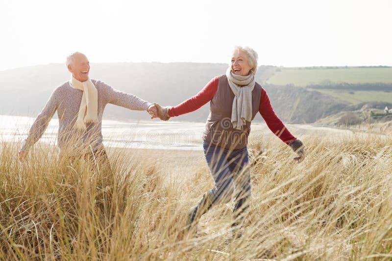 Senior Couple Walking Through Sand Dunes On Winter Beach