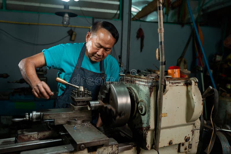 A senior craftsman who is skilled in craftsmanship, is controlling, skillfully operating a lathe, is in a small factory that is royalty free stock image