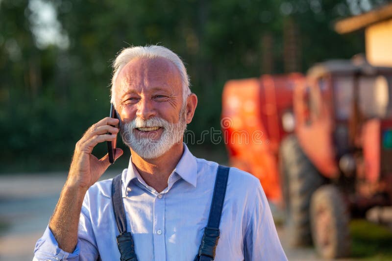 Senior farmer talking on mobile phone in front of tractor