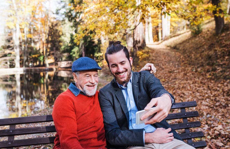 Senior father and his son sitting on bench in nature, taking selfie. royalty free stock images Senior father and his son sitting on bench in nature, taking selfie. royalty free stock images