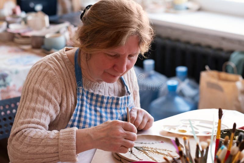 Senior female artist making flower ornament on ceramic product. Concept of ceramic art and hobby at old age stock images