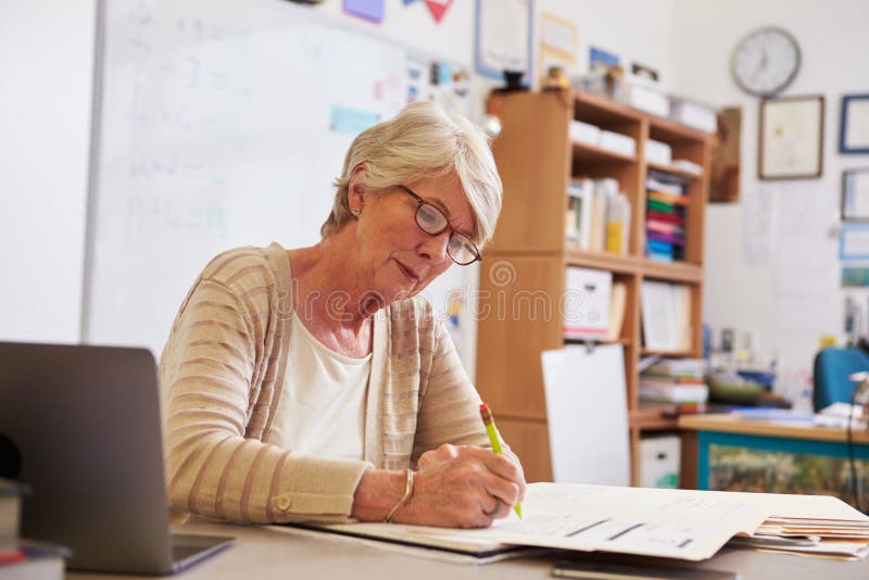 Senior female teacher at her desk marking studentsï¿½ work