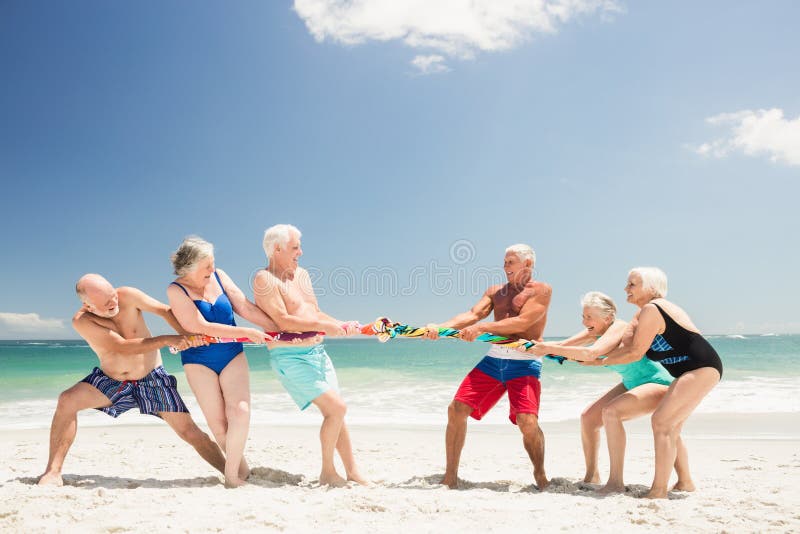Senior friends playing tug of war on the beach