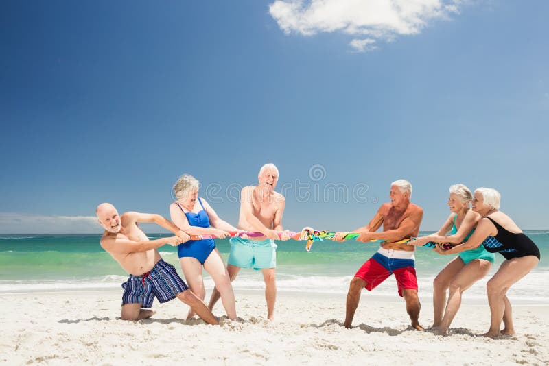 Senior friends playing tug of war on the beach