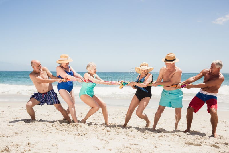 Senior friends playing tug of war on the beach