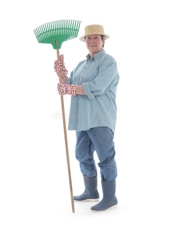 Senior woman gardener wearing straw hat and rubber boots posing with rake over white background. Senior woman gardener wearing straw hat and rubber boots posing with rake over white background