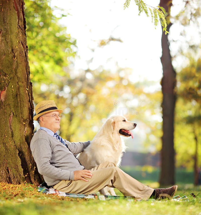 Senior gentleman and his dog sitting on ground in a park