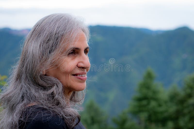 Senior Indian woman with grey hair and glowing skin, meditating in the morning.