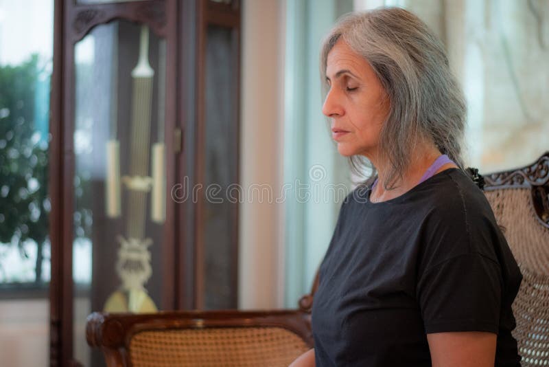Senior Indian woman with grey hair and glowing skin, meditating in the morning.