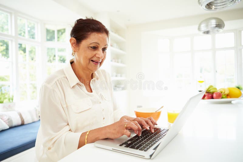 Senior Indian Woman Using Laptop Whilst Eating Breakfast stock photo Senior Indian Woman Using Laptop Whilst Eating Breakfast stock photo