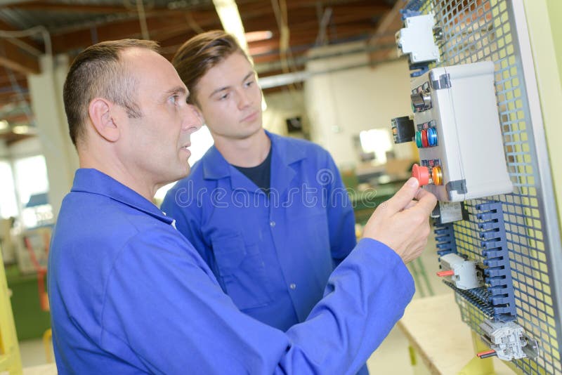 Senior and junior electricians looking at control box