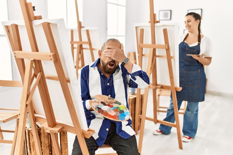 Senior artist man at art studio smiling and laughing with hand on face covering eyes for surprise. blind concept. Senior artist man at art studio smiling and laughing with hand on face covering eyes for surprise. blind concept