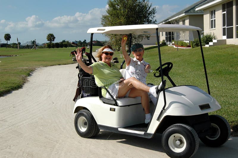 Dve šťastný starších žien máva pri jazde v golfovom vozíku.