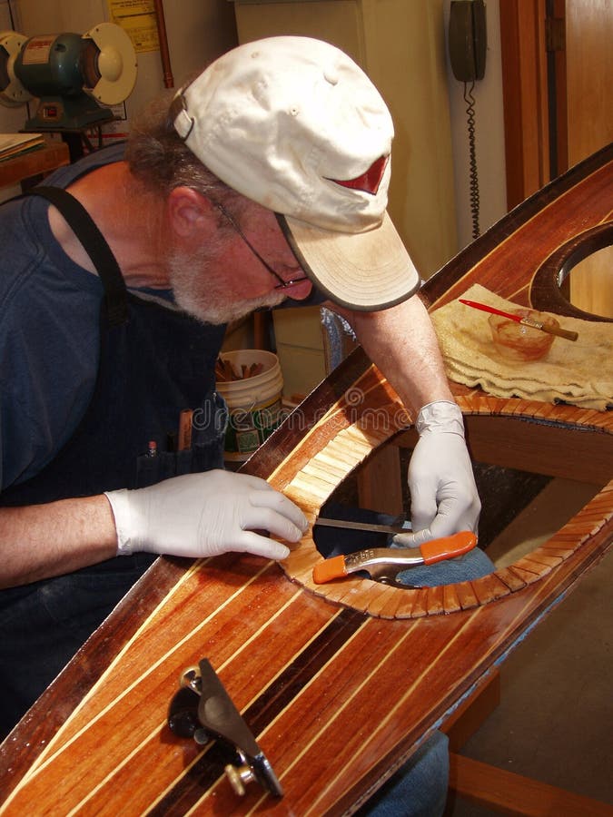 Senior man building wood strip kayak. Laying up hatch stop while working in well-lit shop.