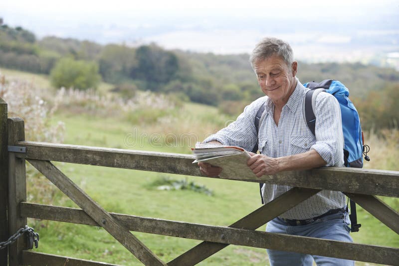 Senior Man Hiking In Countryside Resting By Gate